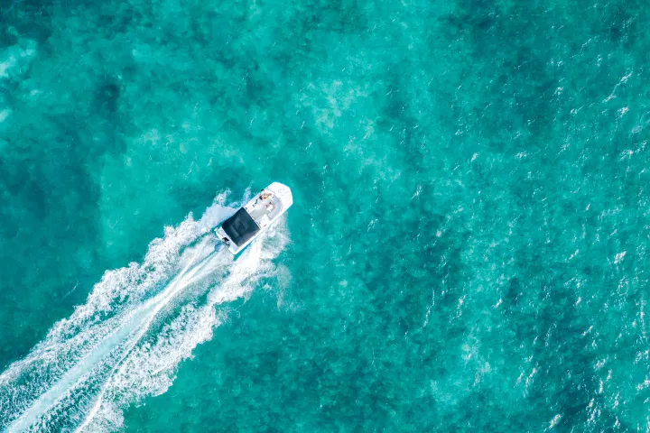 Aerial view of a boat leaving a wake in clear turquoise water.