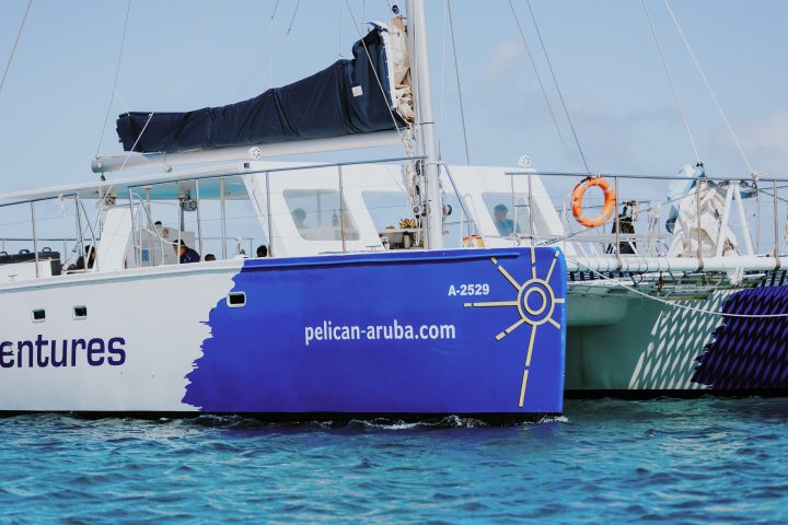 Sailboat on water with 'pelican-aruba.com' and a compass graphic on the side.