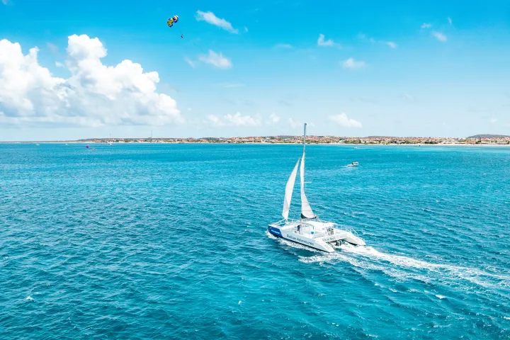 Sailboat cruising on a vast blue ocean under a partly cloudy sky, with land visible in the distance.