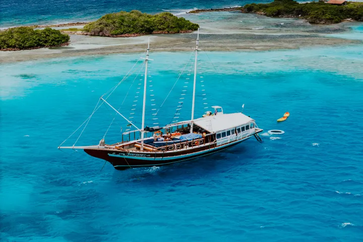 Sailing boat on clear turquoise water near small lush islands.