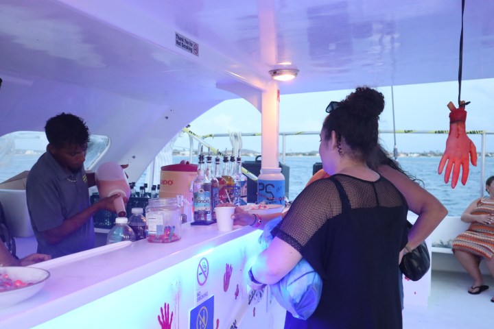 Person at boat bar with drinks and Halloween decorations, including hanging fake hands.
