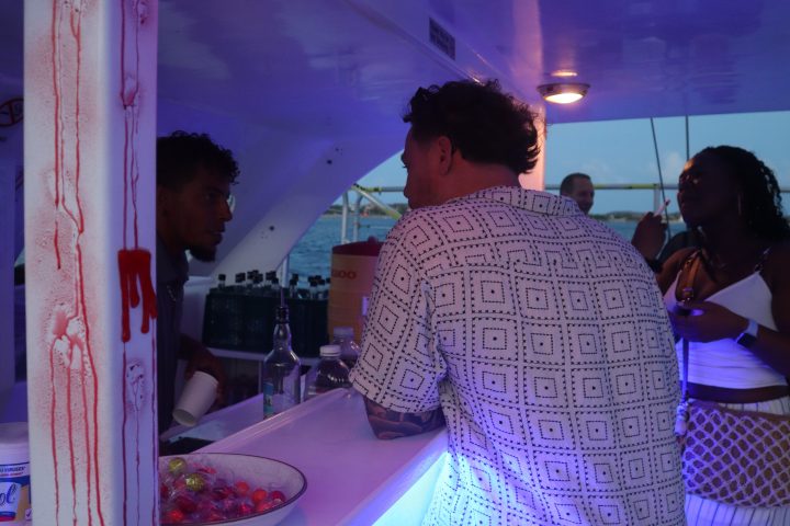 People at a bar with Halloween decor, lit by purple lighting.
