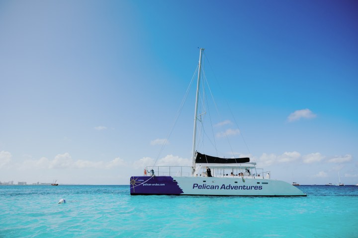 Sailboat with 'Pelican Adventures' on turquoise sea under clear blue sky.
