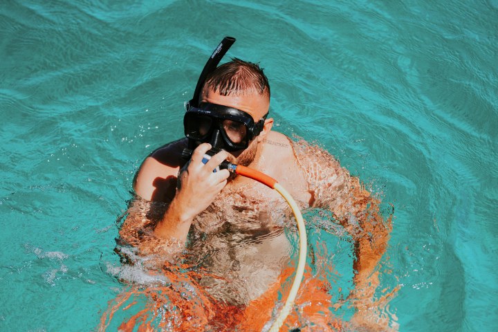 Man in water wearing snorkeling gear and holding a breathing tube.
