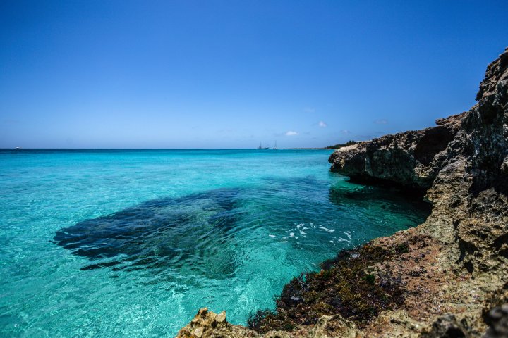 Clear turquoise sea with rocky shoreline under a bright blue sky.