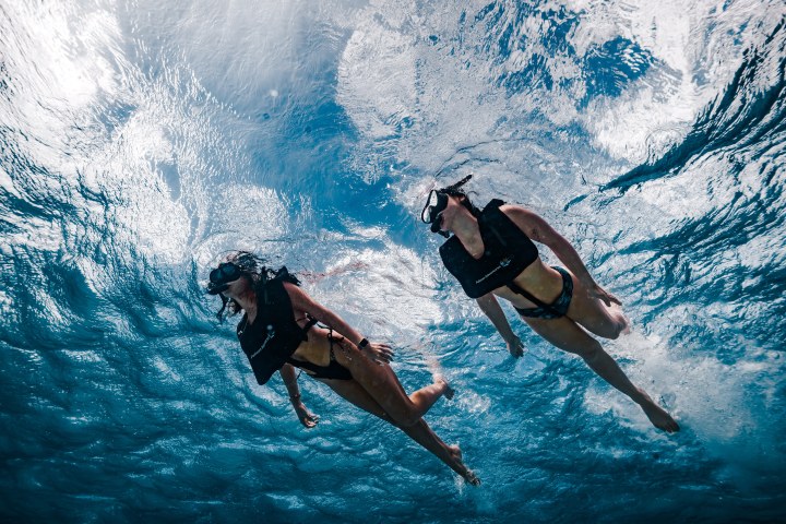 Two people snorkeling underwater with masks and life vests in clear blue ocean.