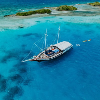 A sailboat anchored near a tropical island with clear blue water and small kayaks nearby.
