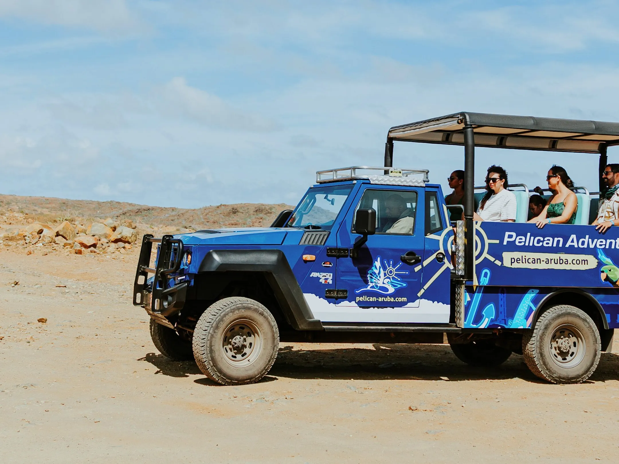 Open jeep tour on a rocky coastline under a blue sky with tourists enjoying the view.