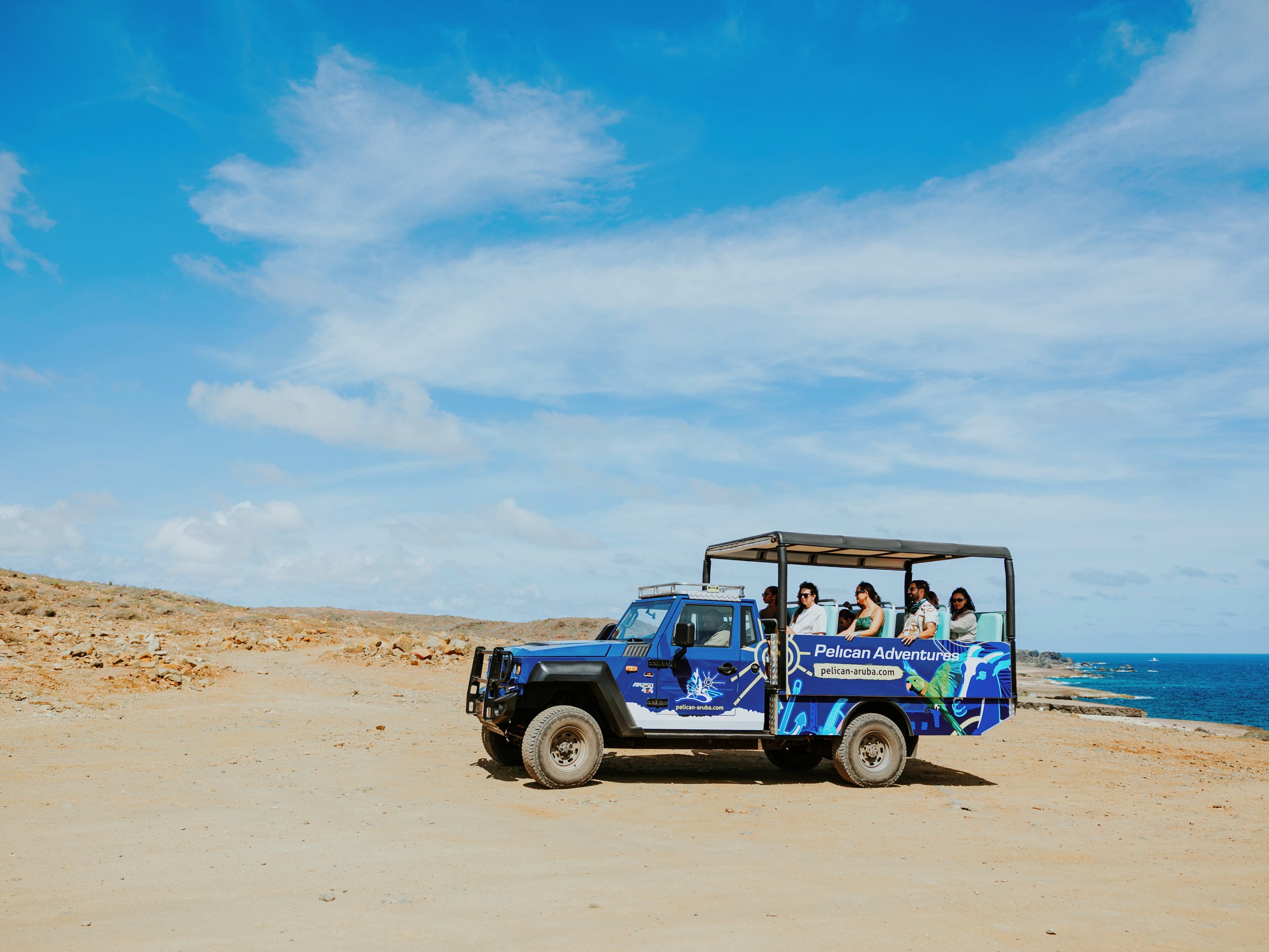 Open jeep tour on a rocky coastline under a blue sky with tourists enjoying the view.