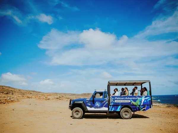 Tourists in an open-top blue safari truck on a desert landscape under a blue sky.