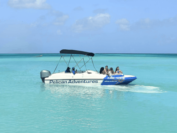 Boat named Pelican Adventures with people on turquoise water under blue sky.